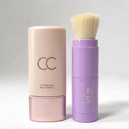 CC tinted serum in a pink bottle beside a purple SPF 30 mineral powder brush with bristles
